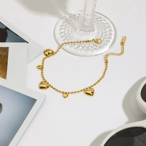 Close-up of golden stainless steel ball chain bracelet with five polished heart charms