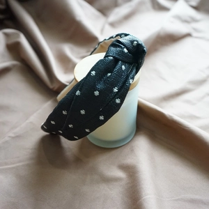 Detail of a black fabric headband with white polka dots and a stylish knot design