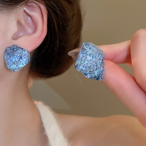 Macro detail of irregular blue resin earrings with silver needles and shimmering glitter