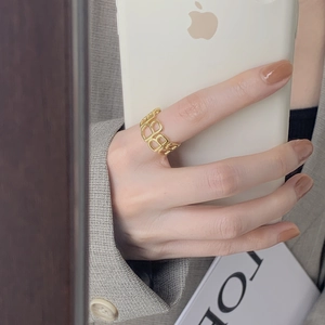 Detail of a gold letter B hollow-out open ring worn on finger with a minimalist background