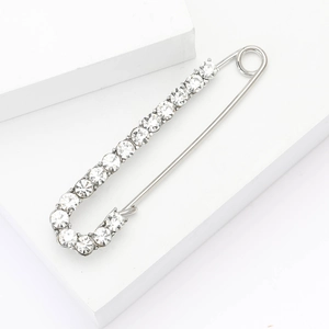 Macro detail of silver safety pin brooch with sparkling crystals on white background