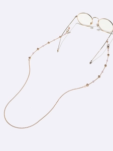 Détail de la chaîne de lunettes dorée avec breloques cœur et perles de nacre