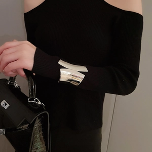 Detail of wide irregular silver cuff bracelet styled with elegant black outfit and bag
