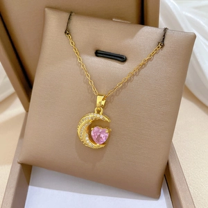 Macro detail of gold moon necklace with pink heart gemstone in a luxury gift box