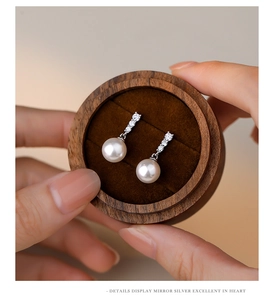 Detailed macro view of S925 silver pearl drop earrings in a walnut jewelry box
