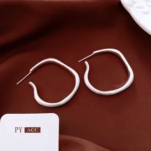 Minimalist silver irregular hoop earrings displayed on deep reddish-brown silk fabric