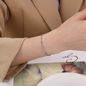 Close-up of a silver cross bracelet with blue beads worn on a wrist with a chic suit