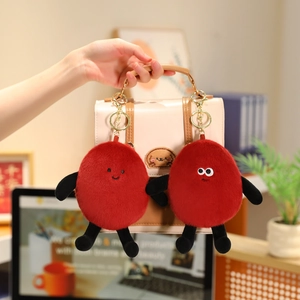 Close-up of red plush peanut charms with golden keychains on a beige handbag