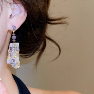 Close-up of dangling purple and white geometric square earrings worn by a model