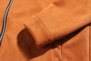 Detailed close-up of faux suede jacket cuff stitching and metal zipper in caramel orange
