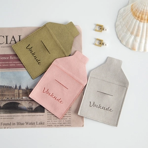 Tres bolsas de microfibra para joyas en verde rosa y gris sobre fondo de papel periódico