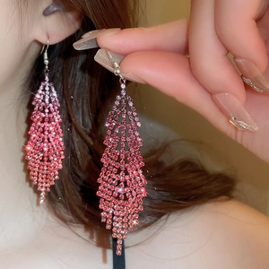 Detailed view of long feather fringe earrings with red gradient rhinestones and silver hooks