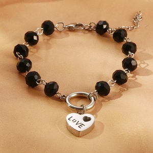 Dettaglio del bracciale di perle nere con un ciondolo a cuore argentato inciso LOVE