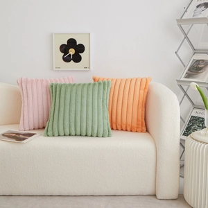 Three colorful plush lumbar pillows in pink, green and orange on a beige sofa