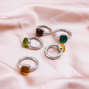 Detail of five colorful square gemstone rings on pink silk with vibrant zircon stones