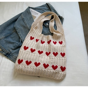 Detalle de bolso de punto con corazones rojos y textura de ganchillo calada en blanco