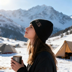 Berretto in maglia nera con risvolto logo su sfondo paesaggistico di montagna innevata