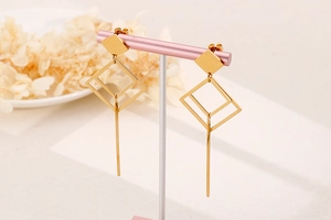 Detail of long geometric gold earrings hanging on display with hollow square pendants