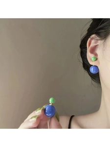 Détail de boucles d'oreilles boules bicolores bleues et vertes sur un mannequin chic