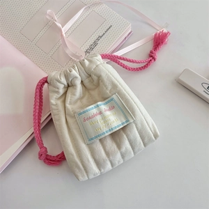 Detailed macro view of quilted cream storage bag with pink drawstring and fringe detail