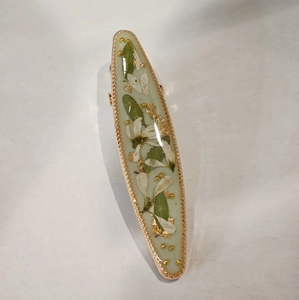Detail of a floral resin hair clip featuring white dried flowers and gold leaf accents