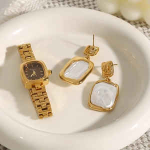 Elegant gold pearl earrings and vintage fashion watch set on a ceramic tray display