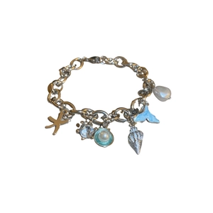 Silver ocean theme charm bracelet with starfish, seashell, whale tail and pearls on white background