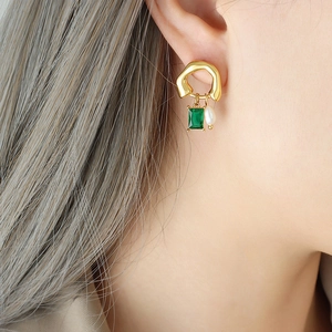 Gold earrings with emerald gemstone and pearl drop shown on a model
