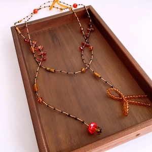 Detailed view of beaded necklace with bow pendant on a wooden tray with amber beads