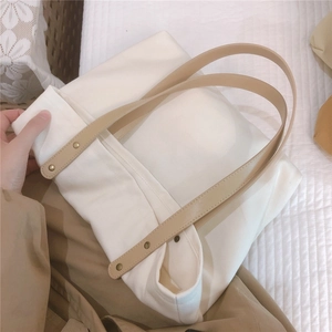 Close-up of white canvas tote bag with khaki leather handles and gold rivet details