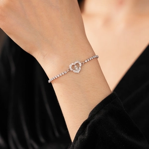 Macro detail of silver heart charm bracelet featuring zircon stones and religious medal