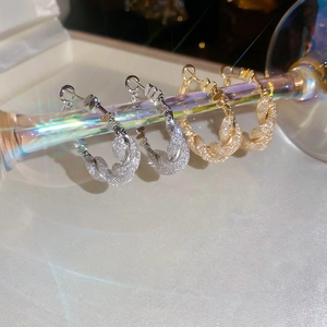 Detail of gold and silver twisted C-shaped earrings with zircons hanging on glass