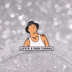 Dettaglio macro della spilla smaltata con testo 'LIFE'S A RISK CARNAL' e stile punk