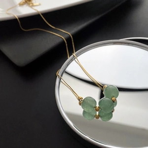 Golden titanium steel necklace with pale green jade beads pendant on mirror background