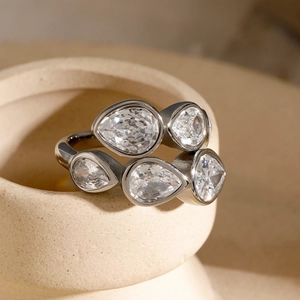 Macro detail of silver pear-cut zircon cross ring on a textured ceramic surface