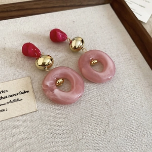 Detailed shot of pink acrylic earrings with gold metal accents on beige linen background