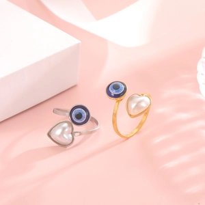 Detail of adjustable ring with heart pearl and blue evil eye charm on pink background