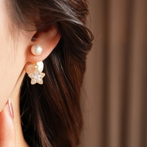 Detail of 18K gold star stud earrings with zircon inlay and textured white pearls on model