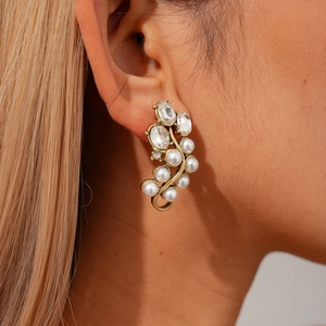 Détail de boucles d'oreilles vintage en or avec perles et strass portées à l'oreille