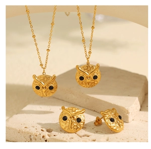 Macro shot of gold owl jewelry set featuring necklaces and earrings on stone background