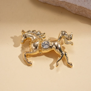 Macro detail of a golden running horse brooch with a round crystal on a beige stone surface