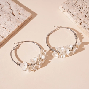 Détail de boucles d'oreilles créoles argentées avec fleurs 3D blanches sur travertin