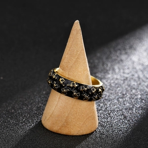 Nahaufnahme eines Punk-Totenkopfrings mit Goldprägung auf einem Holzständer vor grauem Grund
