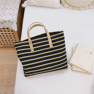 Detail of striped canvas tote bag with leather handles and gold rivet reinforcements