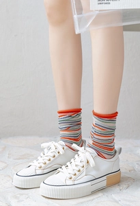 Detail of colorful striped crew socks with orange rolled cuffs and white platform sneakers