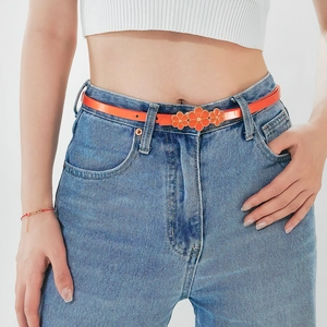 Close-up of orange patent leather belt featuring three floral buckles on denim jeans
