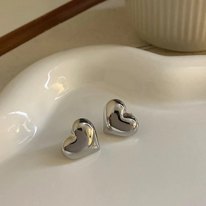Close-up of silver heart-shaped stud earrings on a white heart ceramic tray