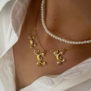 Double-layered gold necklace with crab pendants and white pearl strand on white shirt