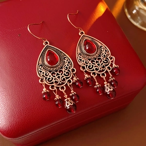 Dettaglio di orecchini vintage in bronzo con pietre rosse e nappe di perline