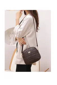 Detail of dark brown quilted crossbody bag with gold butterfly buckle on white suit